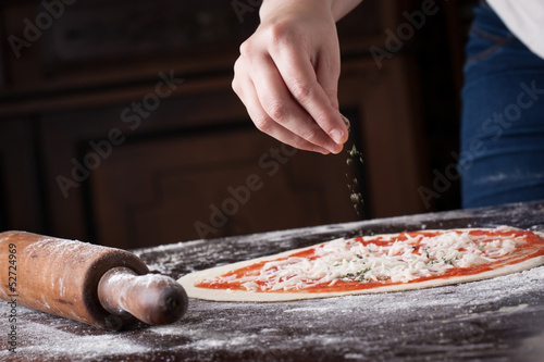 Cook putting oregano on raw pizza