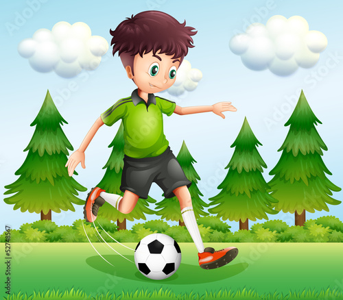 A boy kicking the ball near the pine trees