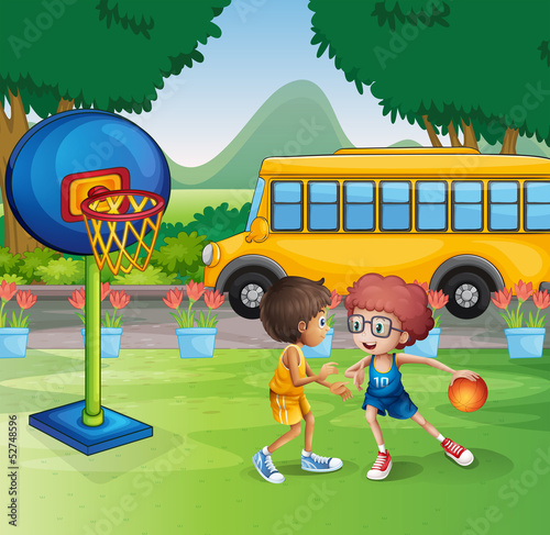 Two boys playing basketball near the school bus