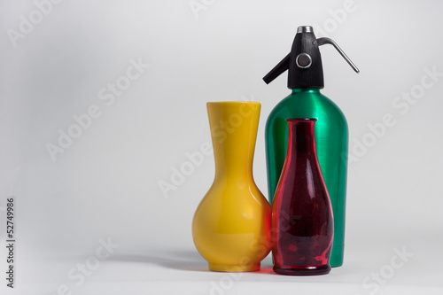 Still life of red bottle yellow vase and green seltzer siphon