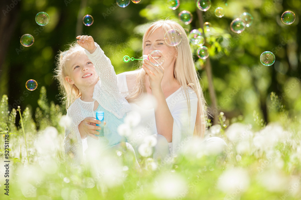 Happy mother and daughter blowing bubbles in the park