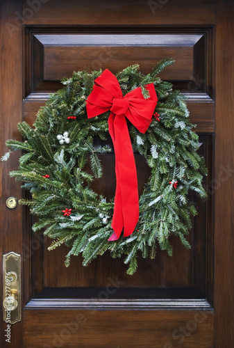 Wooden front door decorated with writh and red bow.