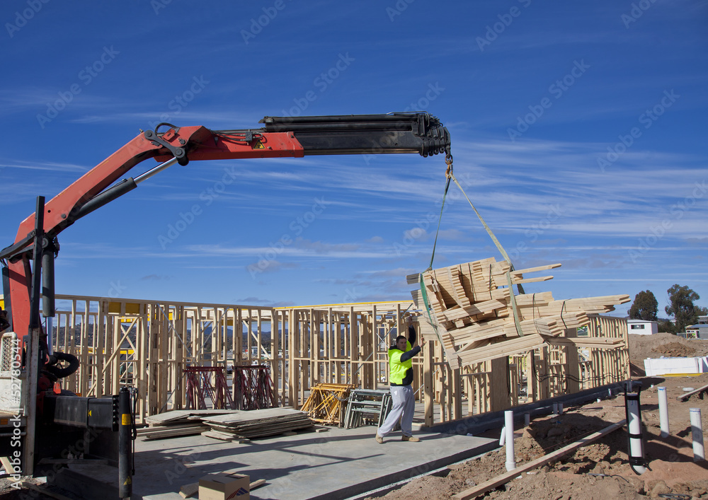 Workman guides load of trusses for housing under construction