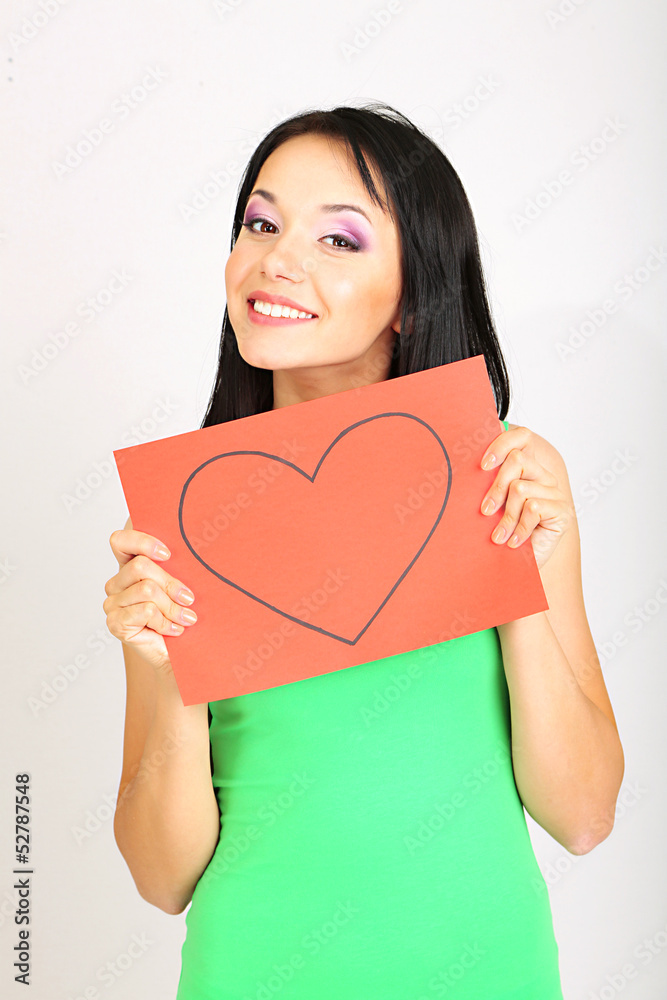 Young woman holding red painted heart on grey background Young woman holding red painted heart on grey background