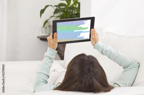 Young woman lying on the couch and working with a digital tablet