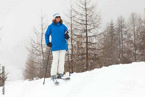 Happy ski woman standing in snow with pine trees.