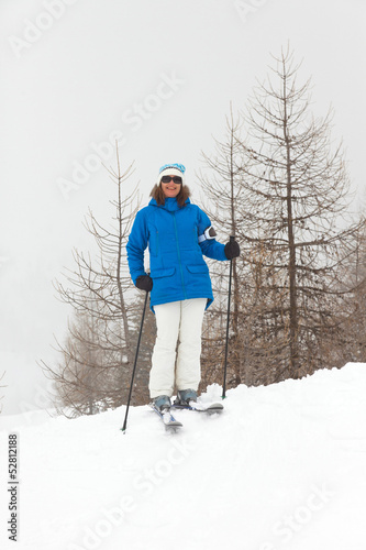 Happy ski woman standing in snow with pine trees.