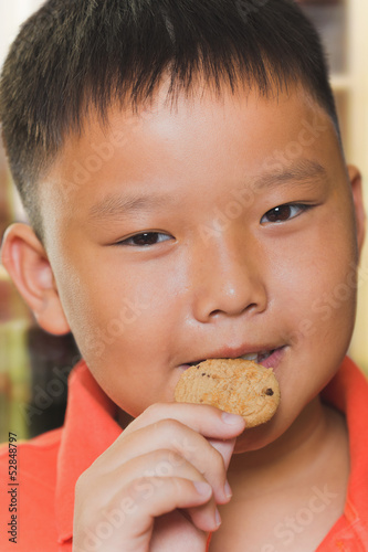 Young asian boy eats a piece of biscuit