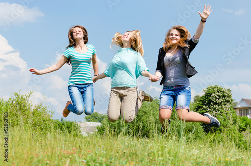 Three happy teen girls friends jumping high in blue sky
