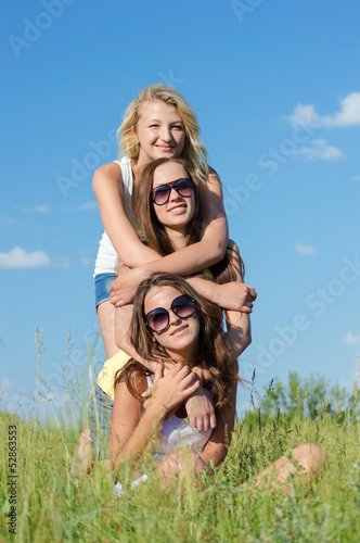 Three happy teen girls embracing against blue sky