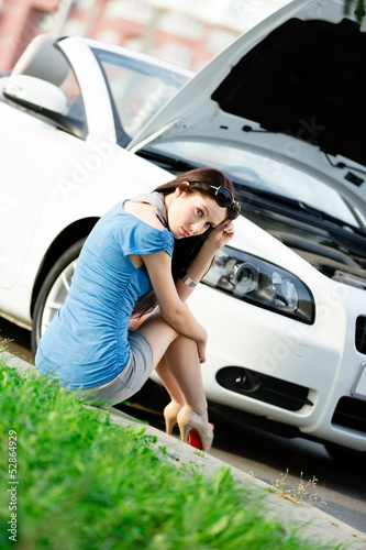 Woman sits on the grass near her broken car © Karramba Production