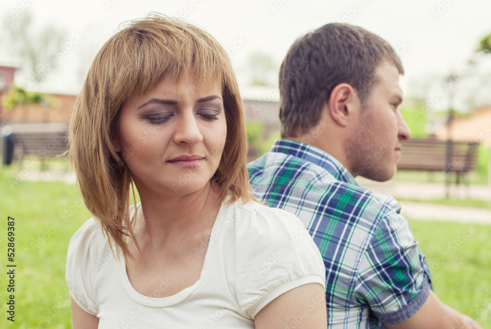 Young couple sitting outdoors on bench bored in relationship Young couple sitting outdoors on bench bored in relationship