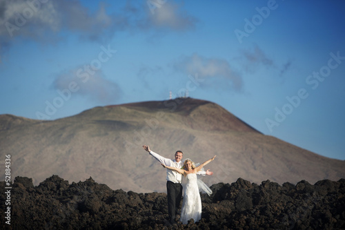 The bride and groom open arms to volcanic landscape background. photo