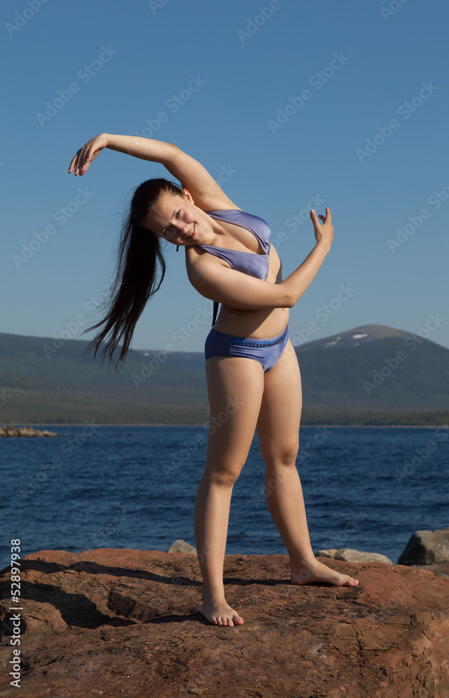 The girl in a bathing suit doing gymnastics on the rock The girl in a bathing suit doing gymnastics on the rock