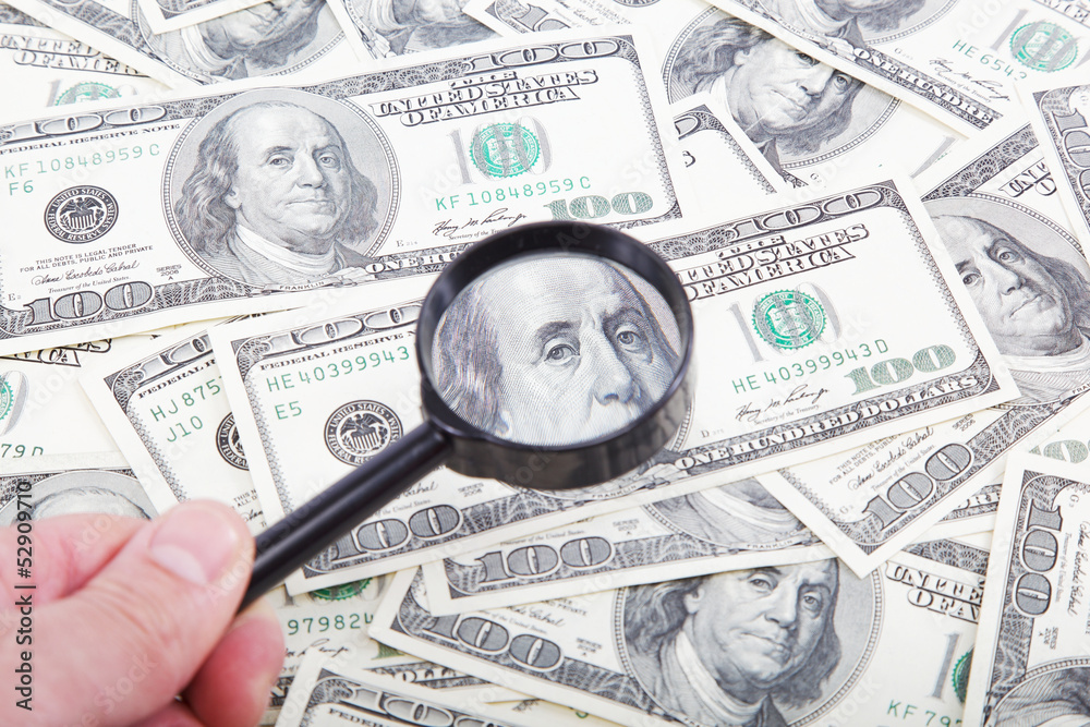 Hand with magnifying glass on a background of dollar bills. Hand with magnifying glass on a background of dollar bills.