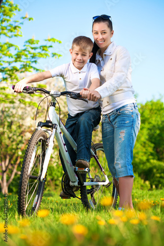 happy mom and son in a green park with a bike