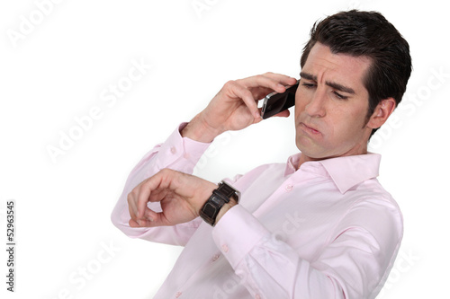 A businessman over the phone looking at his watch.