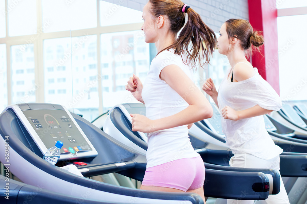 Two young sporty women run on machine Two young sporty women run on machine