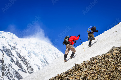 Stampa su tela Two mountain trekkers on snow with peaks background
