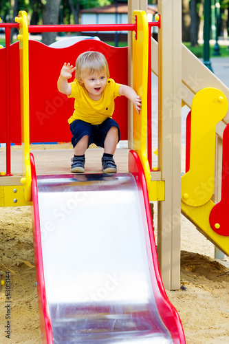 Positive little boy is about to go down from the slide
