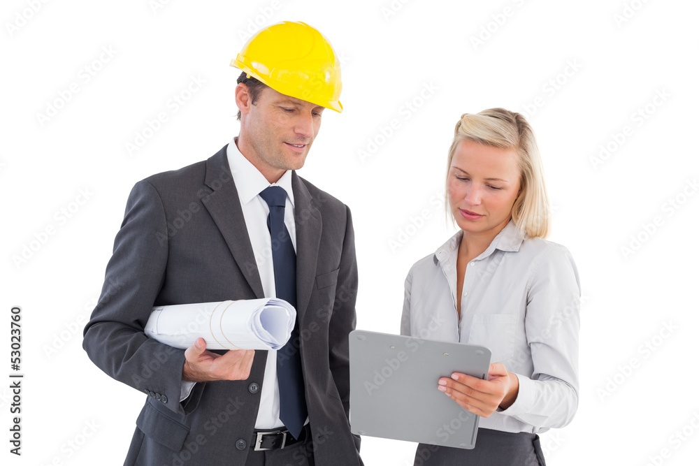 Architects with hard and plans looking at clipboard Architects with hard and plans looking at clipboard