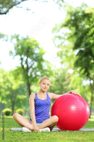 Young female in sportswear sitting on a grass with fitness ball