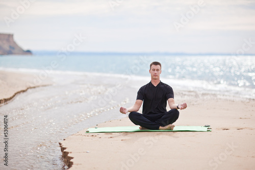 young man doing yoga on the beach