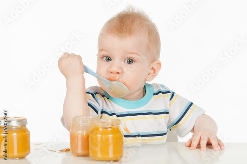 Boy eats with a spoon puree, on a gray background