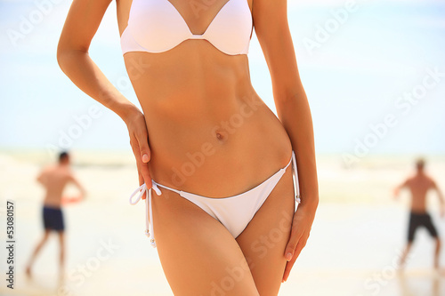 Slim female body and guys playing fresbee on the beach