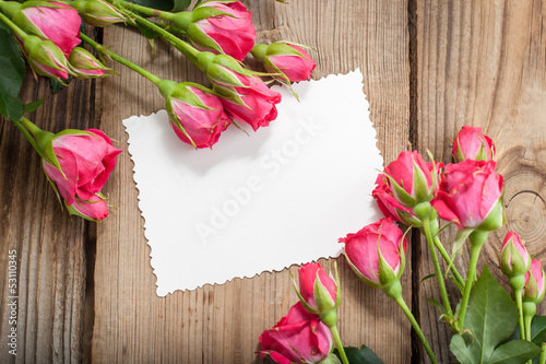 Pink roses and white card with a place for a text on a wooden ta