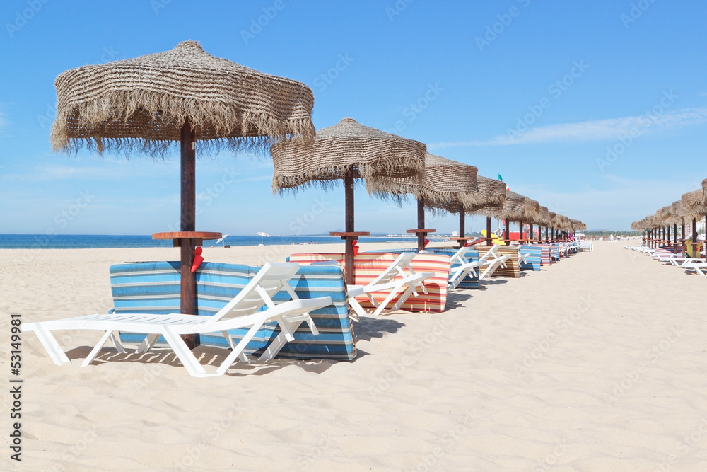 Sunny beach in Portugal with a line of umbrellas near the sea. S