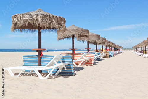 Sunny beach in Portugal with a line of umbrellas near the sea. S