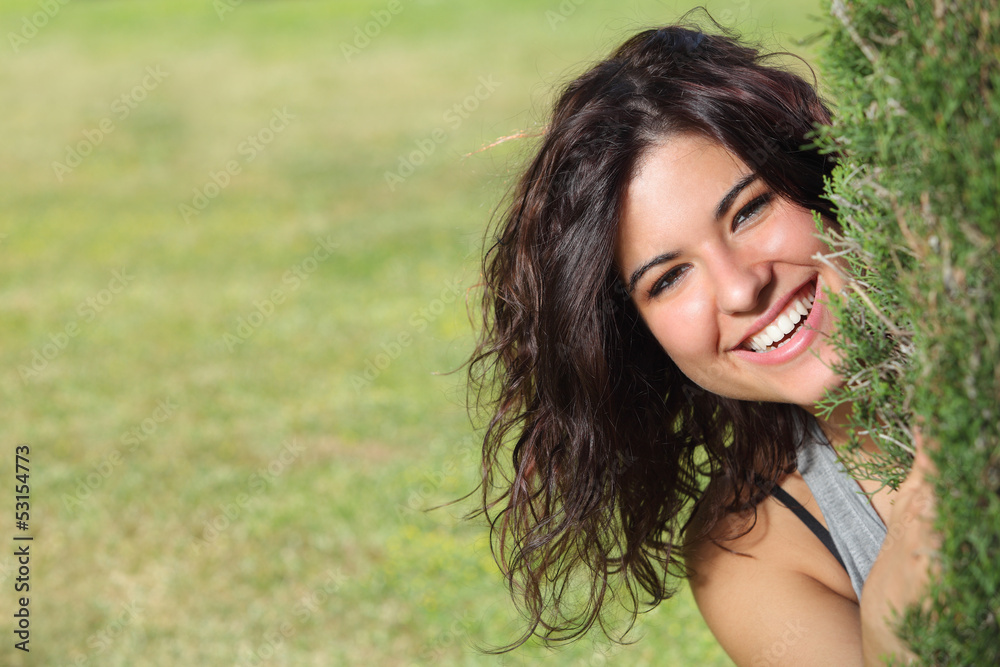 Beautiful woman peeking through a tree and smiling Beautiful woman peeking through a tree and smiling