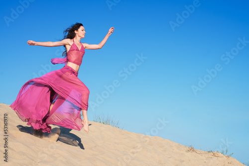 Woman in airy crimson dress running on sand dunes