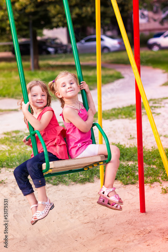 Two beautiful little girls on a swings outdoor in the playground