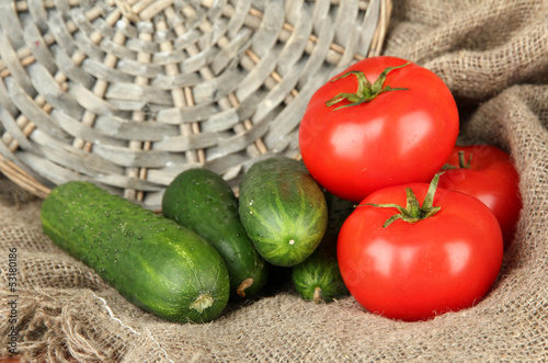 Tasty green cucumbers and red tomatoes on sackcloth background