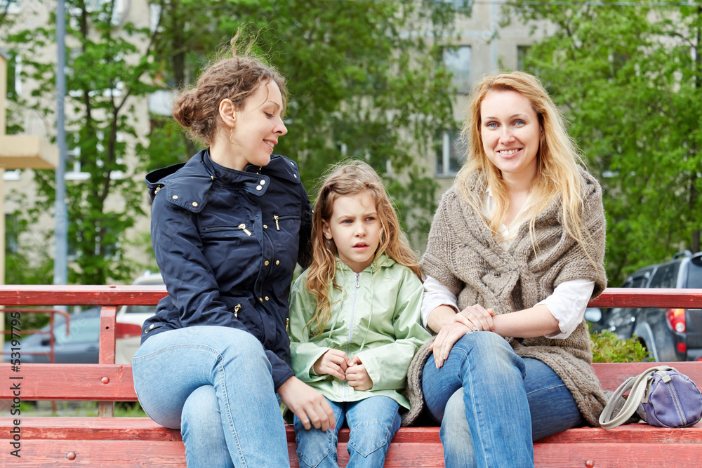 Two young women and little girl sit on bench