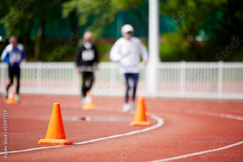 Running track at stadium with runners, focus on cone photo