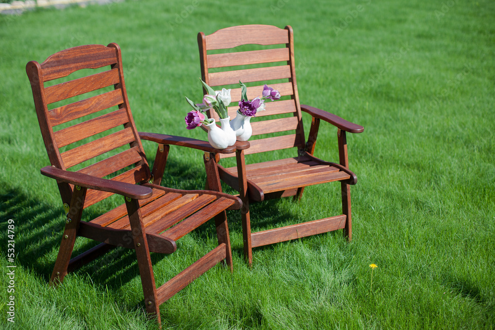 two wood chairs on the grass with vase of flowers on them two wood chairs on the grass with vase of flowers on them