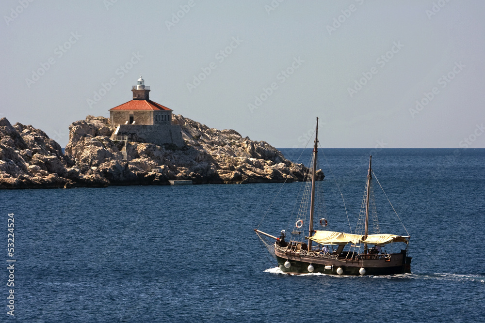 Naklejka premium Lighthouse on the rock near Dubrovnik and old wooden boat