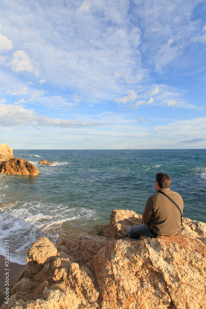 Man sitting on a rock in the beach and looking the sea Man sitting on a rock in the beach and looking the sea