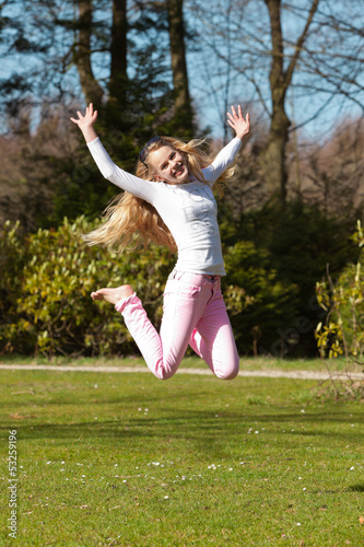 Blonde girl jumping on field of grass in park.