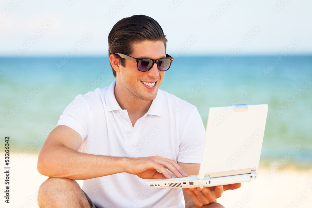 Handsome young man with laptop at beach background