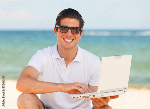 Handsome young man with laptop at beach background