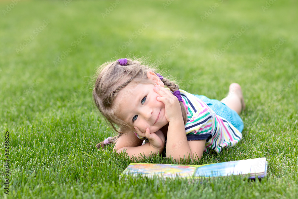 Adorable little girl reading book in the green grass Adorable little girl reading book in the green grass