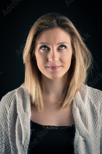 Doubtful blonde woman close up portrait on dark background.