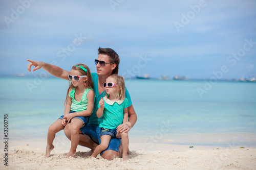 Happy father with his two daughters sitting on tropical beach