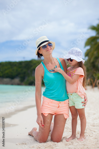 Young mother and her little daughter in hats have fun on beach