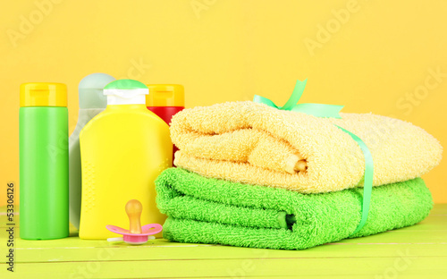 Baby cosmetics and towels on wooden table, on yellow background