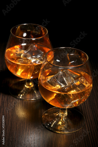 Brandy glasses with ice on wooden background
